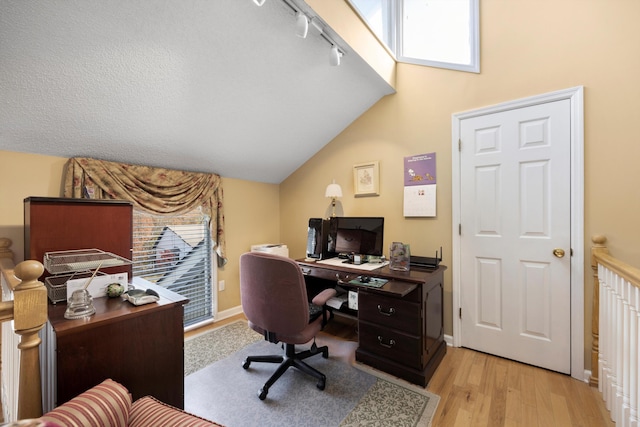 home office featuring lofted ceiling, rail lighting, light wood-style floors, a textured ceiling, and baseboards