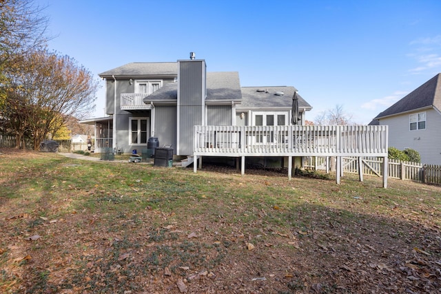 back of property with a yard, a chimney, fence, a deck, and a balcony