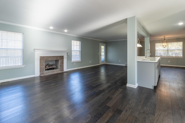 unfurnished living room featuring crown molding, sink, dark hardwood / wood-style floors, a fireplace, and a chandelier