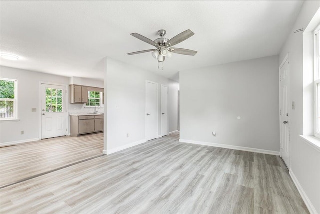 unfurnished living room with light wood finished floors, a sink, ceiling fan, and baseboards