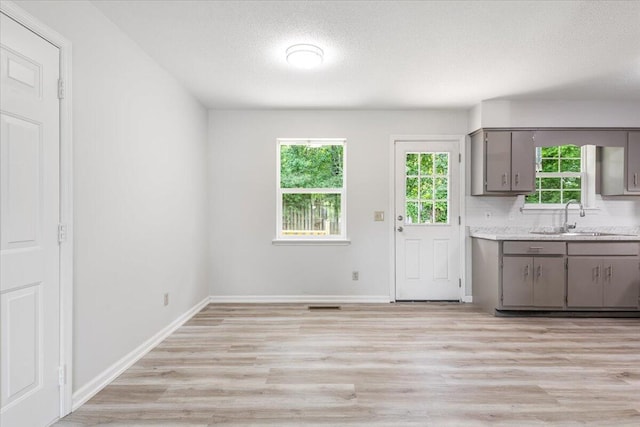 kitchen featuring gray cabinetry, a sink, a textured ceiling, light wood-style flooring, and light countertops