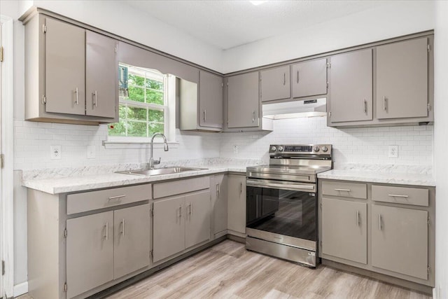 kitchen with stainless steel range with electric cooktop, under cabinet range hood, a sink, and gray cabinetry