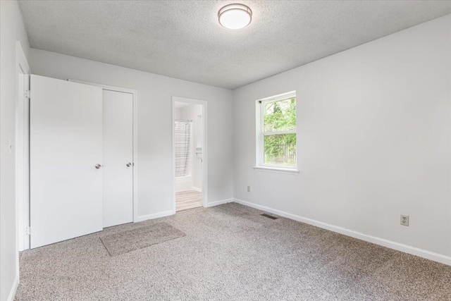 unfurnished bedroom with carpet, a textured ceiling, baseboards, a closet, and ensuite bath