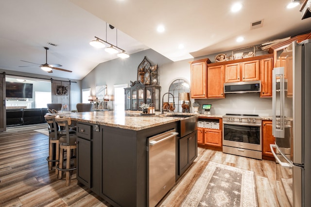 kitchen with appliances with stainless steel finishes, ceiling fan, a center island with sink, decorative light fixtures, and lofted ceiling