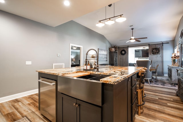 kitchen featuring light stone countertops, vaulted ceiling, a kitchen island with sink, ceiling fan, and a barn door