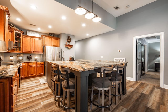 kitchen with light stone counters, light hardwood / wood-style flooring, decorative light fixtures, a kitchen bar, and a kitchen island with sink