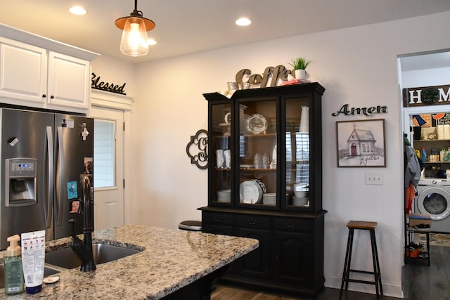 kitchen featuring dark wood-type flooring, stainless steel fridge with ice dispenser, light stone counters, washer / dryer, and white cabinetry