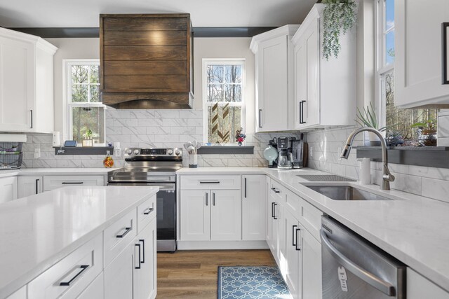 kitchen featuring custom exhaust hood, white cabinets, sink, decorative backsplash, and appliances with stainless steel finishes