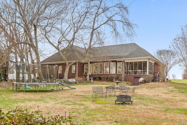 back of house featuring a sunroom, a fire pit, a trampoline, and a yard