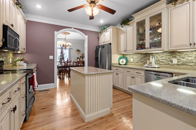 kitchen with stainless steel appliances, light stone counters, crown molding, cream cabinets, and decorative backsplash