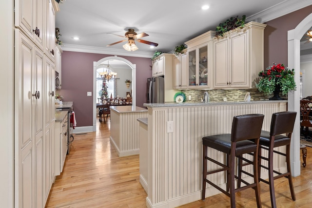 kitchen featuring a kitchen bar, appliances with stainless steel finishes, decorative backsplash, ornamental molding, and cream cabinets