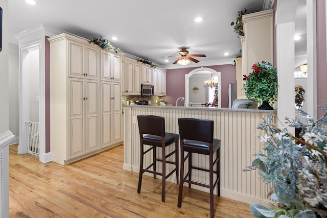 kitchen featuring cream cabinetry, a breakfast bar, kitchen peninsula, and tasteful backsplash