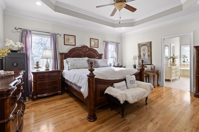 bedroom featuring ceiling fan, light wood-type flooring, ensuite bathroom, and a tray ceiling