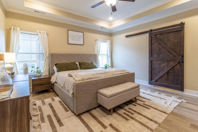 bedroom featuring ceiling fan, a barn door, light wood-type flooring, and a raised ceiling