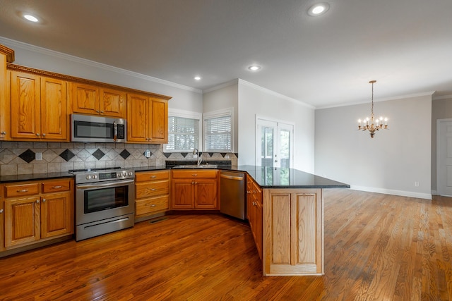 kitchen with kitchen peninsula, appliances with stainless steel finishes, ornamental molding, wood-type flooring, and a chandelier