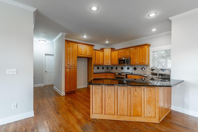 kitchen featuring sink, backsplash, kitchen peninsula, appliances with stainless steel finishes, and ornamental molding