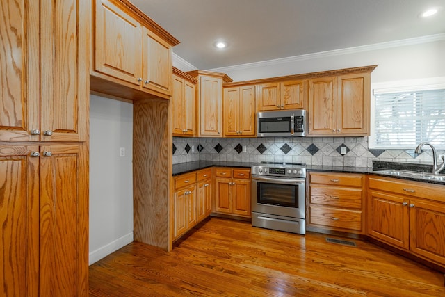 kitchen with appliances with stainless steel finishes, tasteful backsplash, dark stone counters, crown molding, and sink