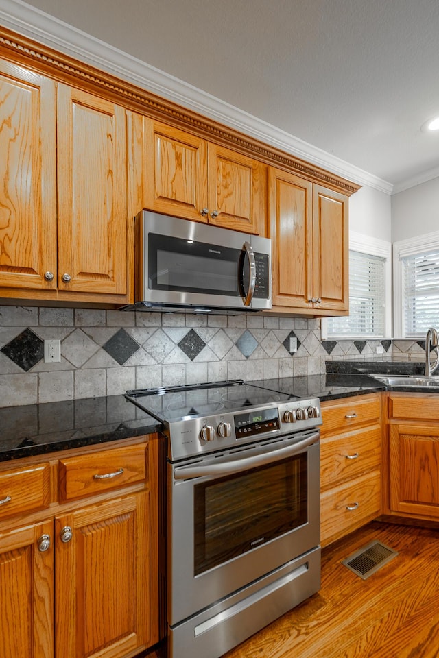 kitchen with decorative backsplash, ornamental molding, stainless steel appliances, sink, and dark stone countertops