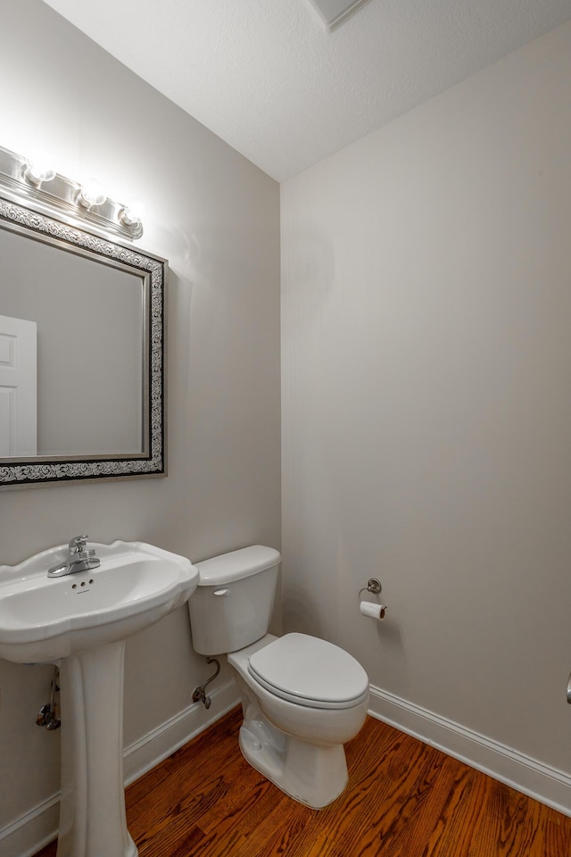 bathroom with hardwood / wood-style flooring, sink, toilet, and a textured ceiling