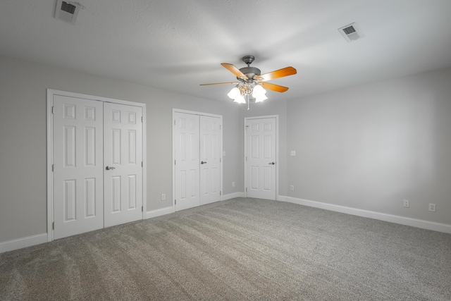 unfurnished bedroom with carpet flooring, ceiling fan, and two closets