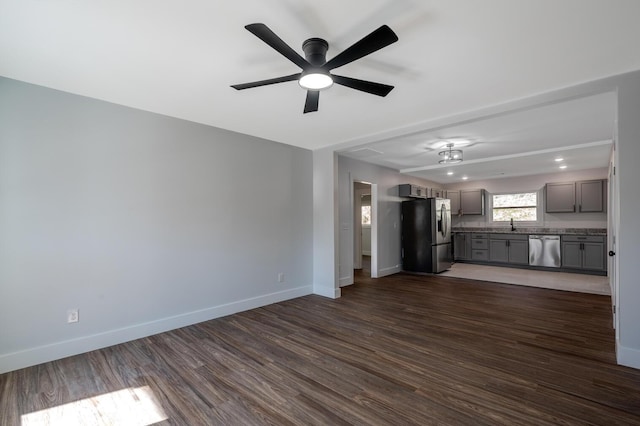 unfurnished living room with ceiling fan, sink, and dark wood-type flooring