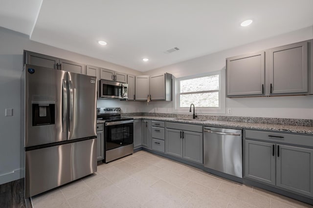 kitchen featuring gray cabinets, light stone counters, sink, and appliances with stainless steel finishes