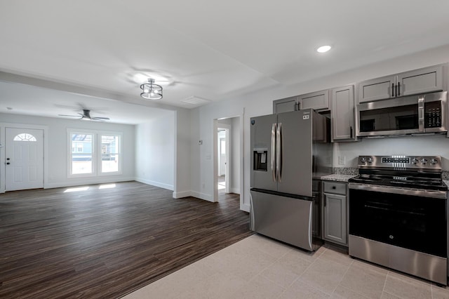 kitchen with appliances with stainless steel finishes, light stone counters, ceiling fan, light hardwood / wood-style flooring, and gray cabinets