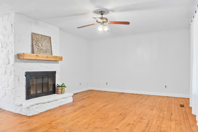 unfurnished living room with hardwood / wood-style floors, a stone fireplace, ceiling fan, and crown molding