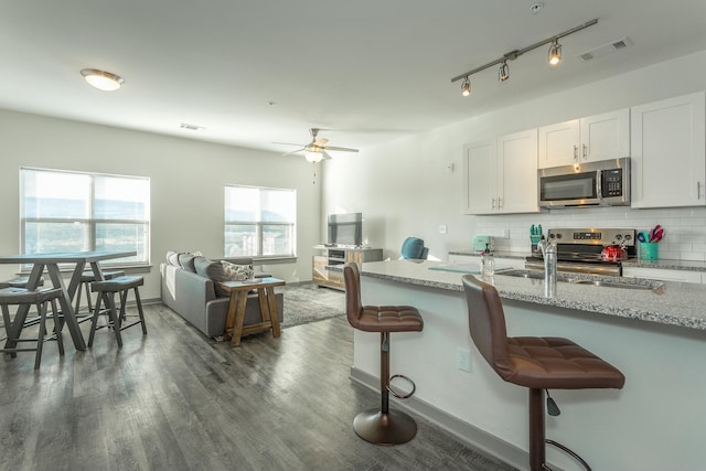 kitchen with white cabinetry, light stone countertops, decorative backsplash, a breakfast bar, and appliances with stainless steel finishes