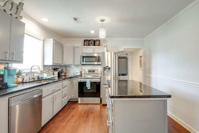 kitchen with stainless steel appliances, crown molding, sink, hardwood / wood-style flooring, and hanging light fixtures