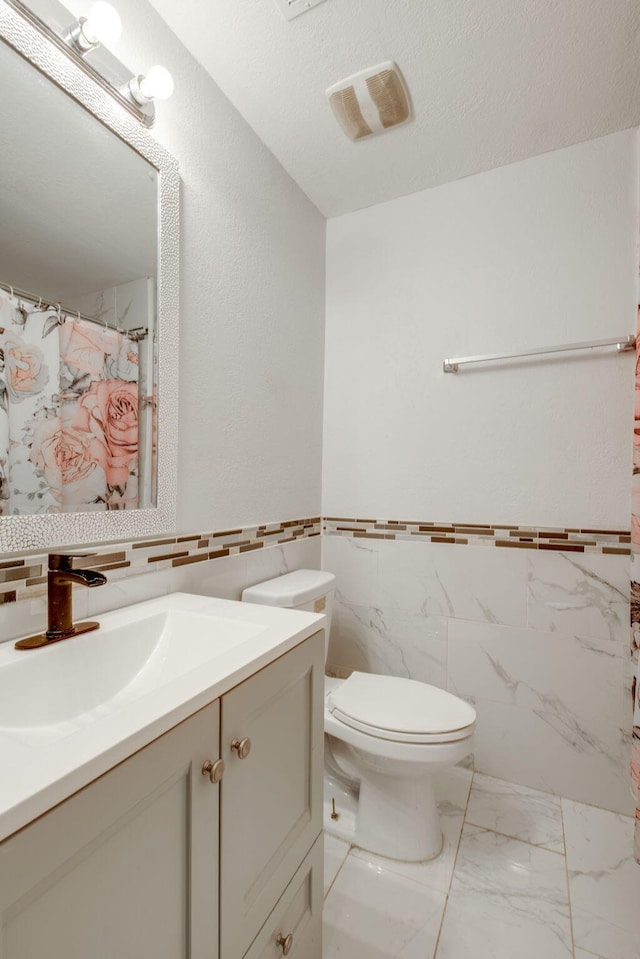 bathroom featuring a textured ceiling, vanity, tile walls, and toilet