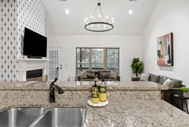 kitchen featuring light stone countertops, sink, pendant lighting, a chandelier, and lofted ceiling