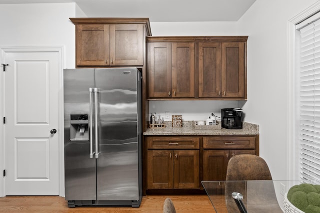 kitchen with stainless steel fridge with ice dispenser, light hardwood / wood-style flooring, and stone countertops