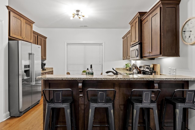 kitchen with a kitchen breakfast bar, light wood-type flooring, appliances with stainless steel finishes, light stone counters, and kitchen peninsula