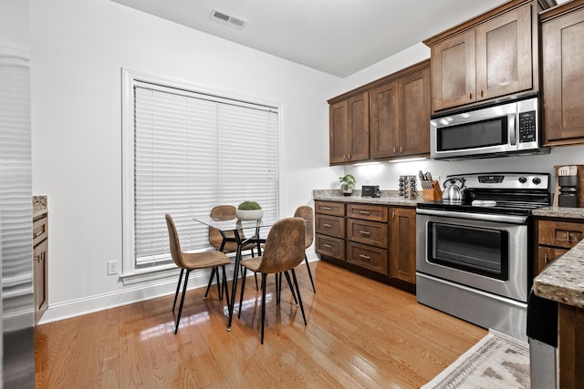 kitchen with light wood-type flooring, stainless steel appliances, light stone counters, and dark brown cabinetry