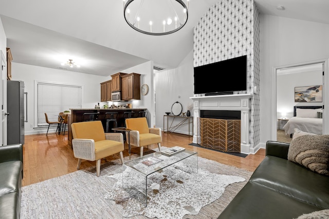 living room with a chandelier, light wood-type flooring, a large fireplace, and high vaulted ceiling