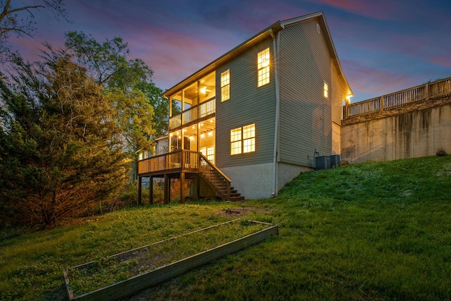 back house at dusk featuring a lawn and a balcony