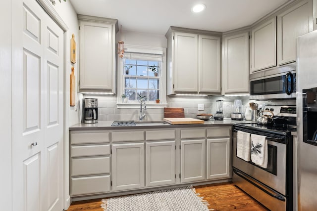 kitchen featuring sink, decorative backsplash, gray cabinets, light wood-type flooring, and appliances with stainless steel finishes