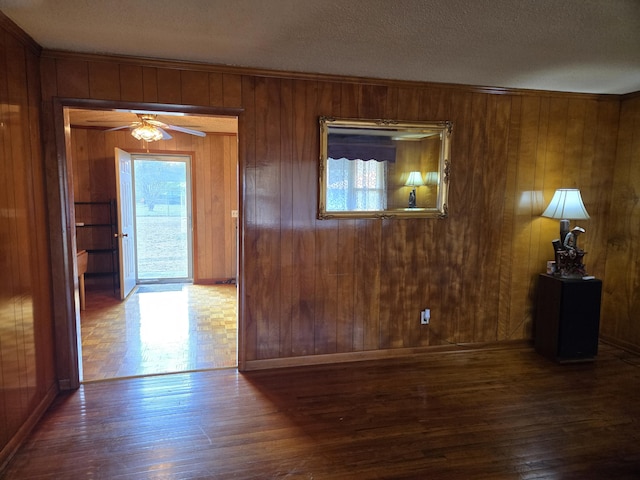 interior space featuring wood walls, ceiling fan, dark wood-type flooring, and a textured ceiling