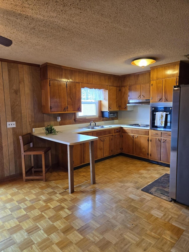 kitchen featuring stainless steel fridge, gas stovetop, wall oven, kitchen peninsula, and a breakfast bar area