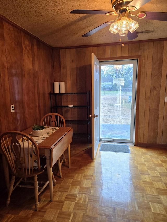 dining space with ceiling fan, wood walls, a textured ceiling, and light parquet floors