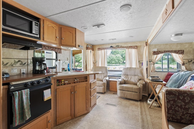 kitchen featuring stainless steel microwave, sink, wall oven, range hood, and a textured ceiling