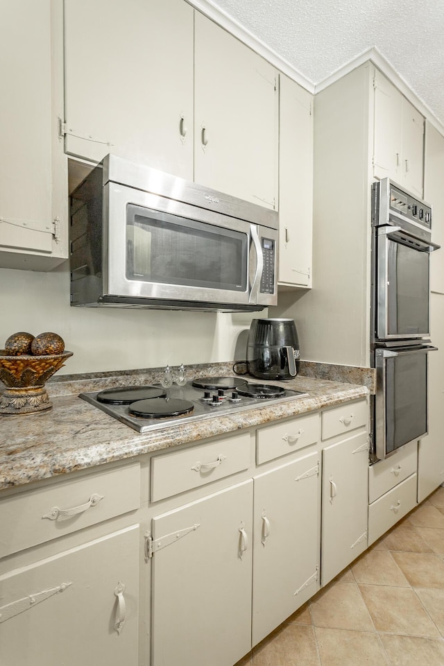 kitchen featuring cooktop, a textured ceiling, black double oven, light tile patterned floors, and white cabinets