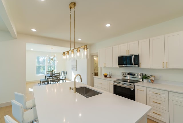 kitchen with stainless steel appliances, a kitchen island with sink, sink, white cabinets, and hanging light fixtures