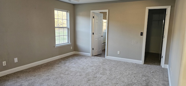 unfurnished bedroom with a walk in closet, baseboards, carpet, ensuite bathroom, and a closet