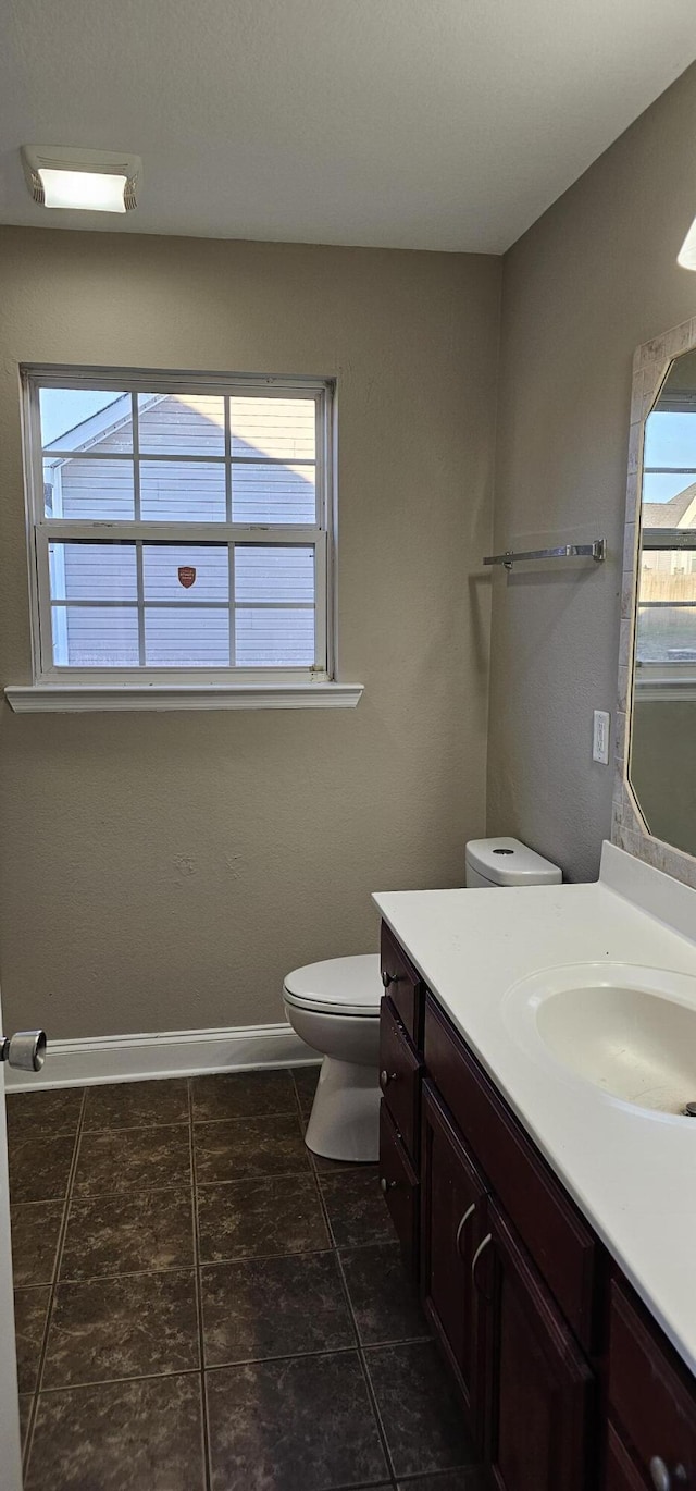 bathroom featuring a healthy amount of sunlight, toilet, vanity, and baseboards