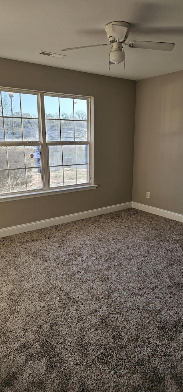 carpeted spare room with visible vents, baseboards, and a ceiling fan