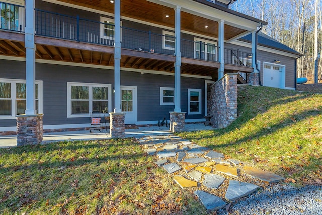 rear view of property with a garage, a lawn, and a balcony