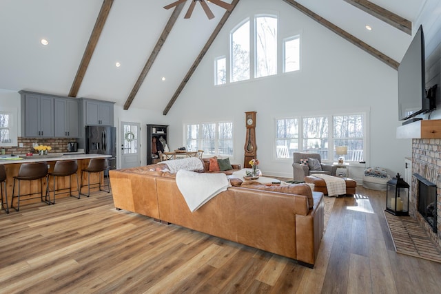 living room featuring a brick fireplace, high vaulted ceiling, ceiling fan, and light wood-type flooring