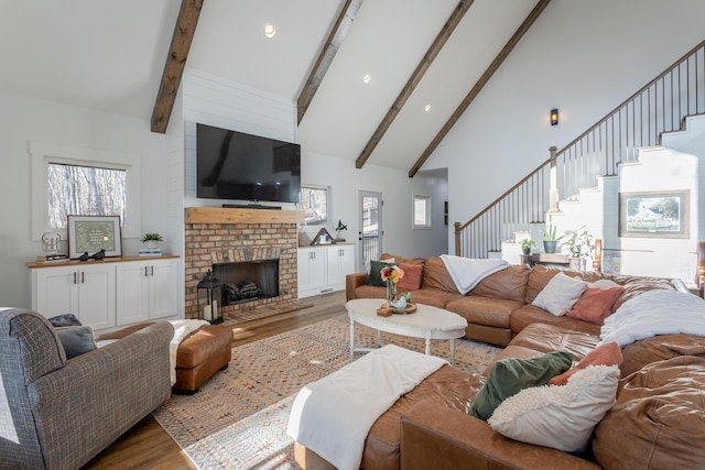 living room featuring beamed ceiling, a brick fireplace, high vaulted ceiling, and light hardwood / wood-style flooring